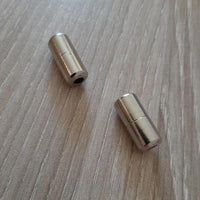 Gros plan sur deux embouts métalliques pour lacets élastiques, permettant un laçage sans nœud