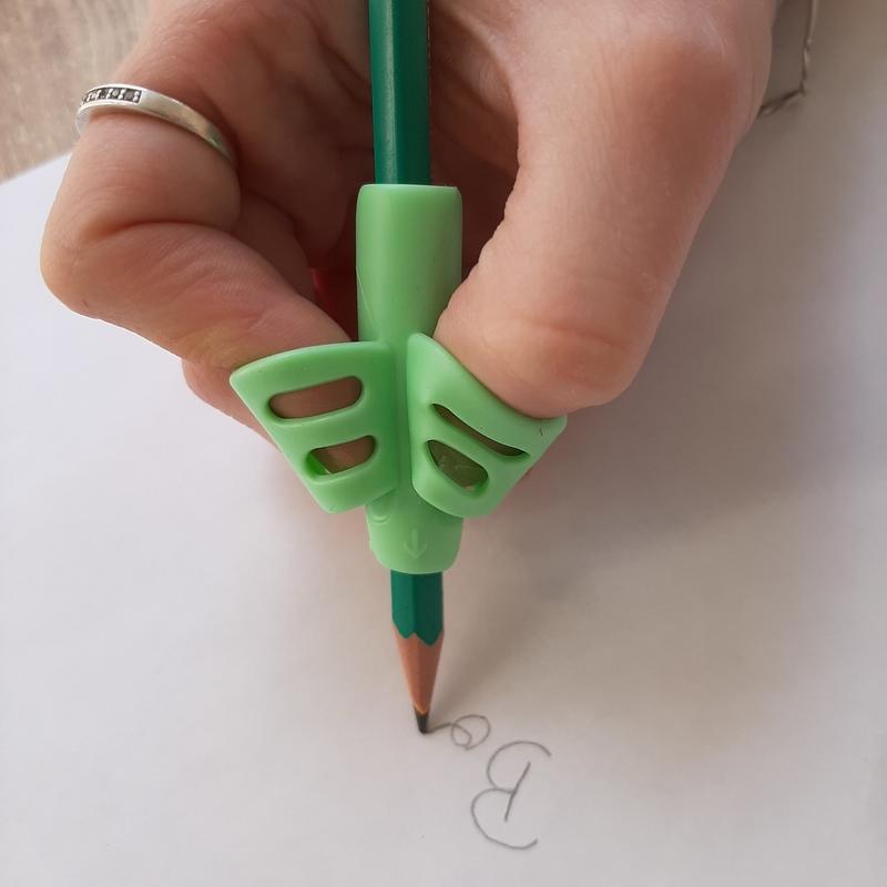 Guide doigt vert en silicone posé sur un stylo, positionnant le pouce et l'index pendant l'écriture