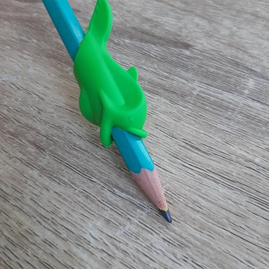 Guide doigt poisson vert fixé sur un crayon, positionnant les doigts pour l'écriture